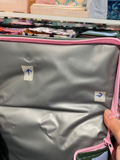 Lid lining of the Imperfect Mini tote with an arrow sticker pointing to crescent moon shaped fold approx 10mm wide, and the 2 tiny cuts approx 1mm each near the zipper on the right side.