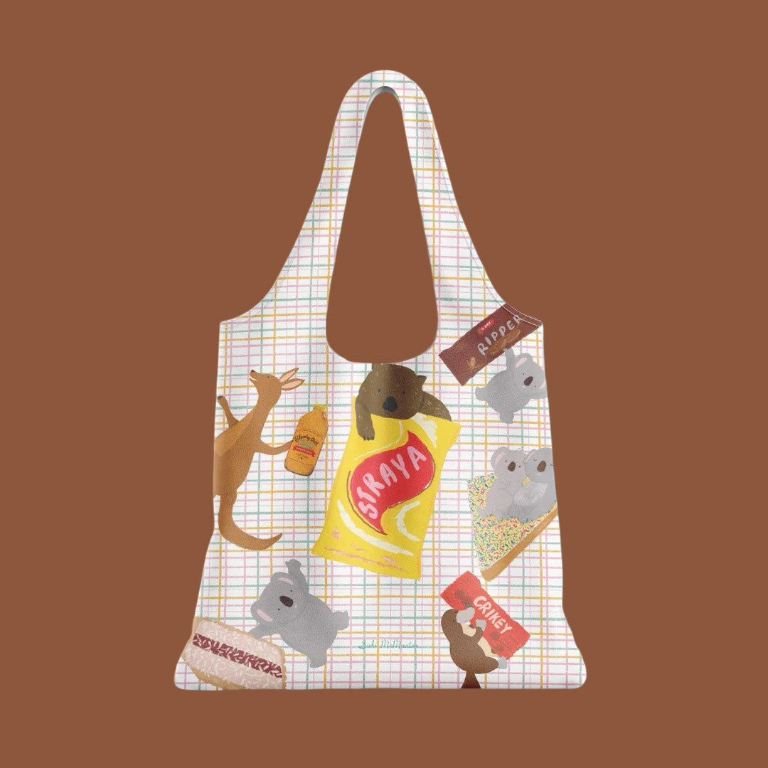 A reusable shopping tote bag with a white grid background and a playful Aussie snack-themed illustration featuring cartoon animals and Aussie slang like 'Straya' and 'Crikey'.