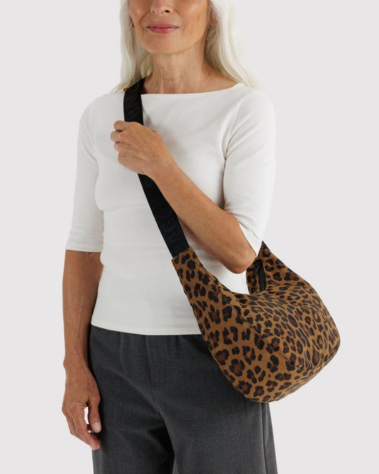 A woman wearing a white top and dark grey pants carries a leopard-print shoulder bag with a black strap against a white background.