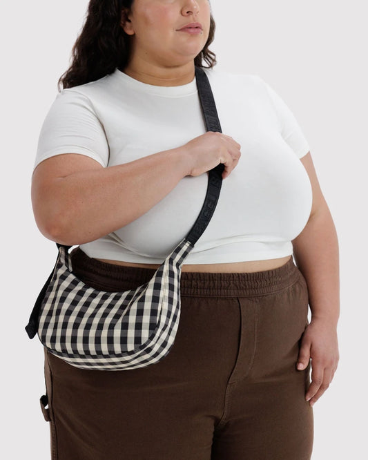 Person wearing a white top and brown pants with a black and white checkered bag over their shoulder on a white background