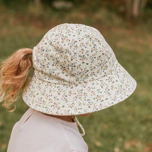 Side view of child wearing a floral bucket hat with a ponytail slit in the back, in an outdoor setting