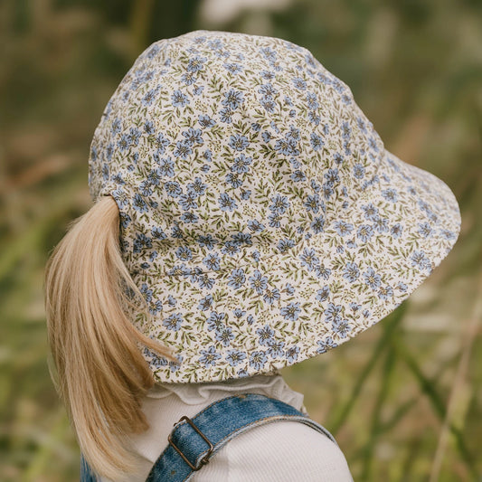 Back view of Child wearing a floral-patterned hat with a ponytail slit in the back in a natural setting