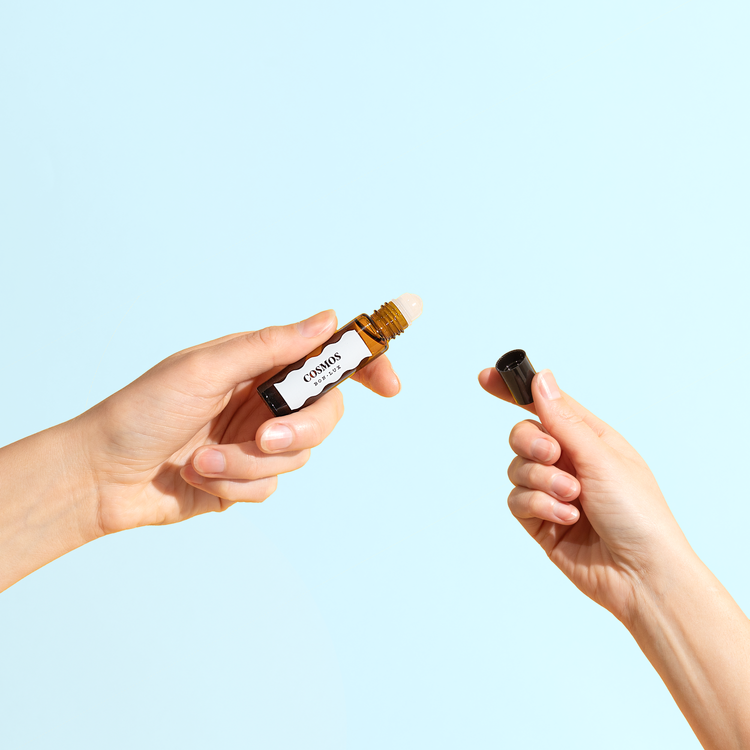 A pair of hands holding a bottle of Bon Lux Cosmos Natural Perfume in one hand and the lid in the other hand.