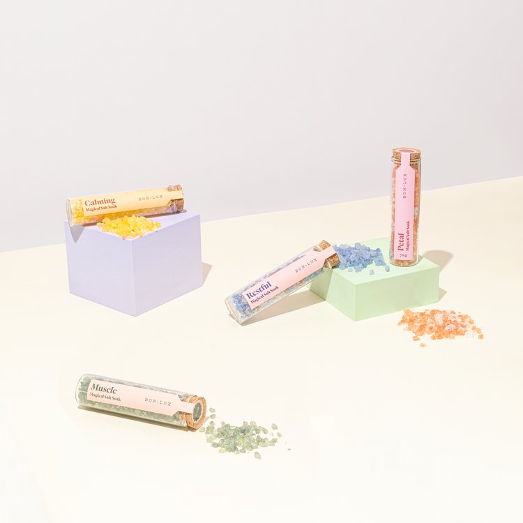 Tubes of Bon Lux Magical Salt Soak on a light surface with sprinkles of each salt
