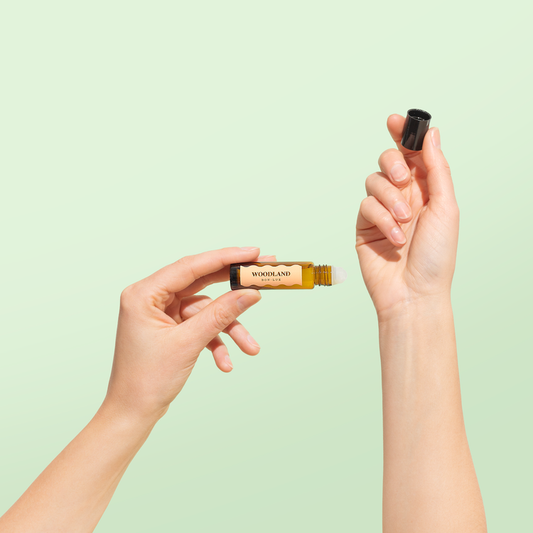 A pair of hands holding a bottle of Box Lux Woodland Natural Perfume in one hand and another holding the lid of the bottle