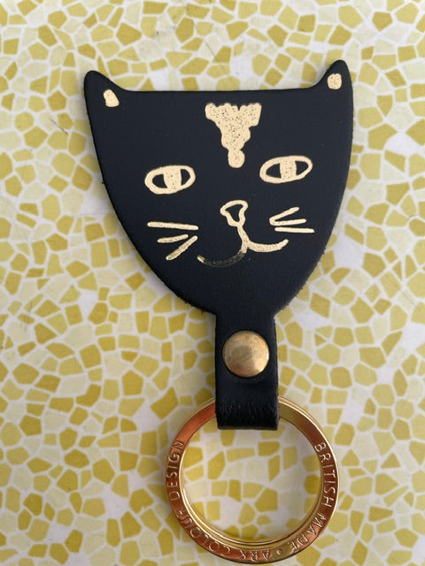 Close up of IMPERFECT art cat key fob in black. Missing a section of gold foil on the smile line.