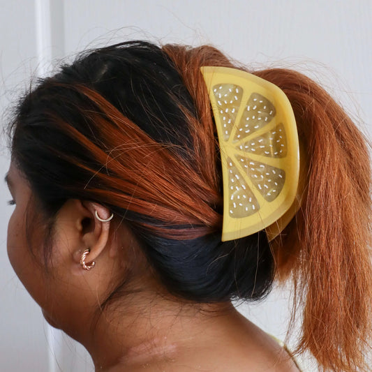 Person with a giant yellow lemon slice hair claw in their hair against a white background