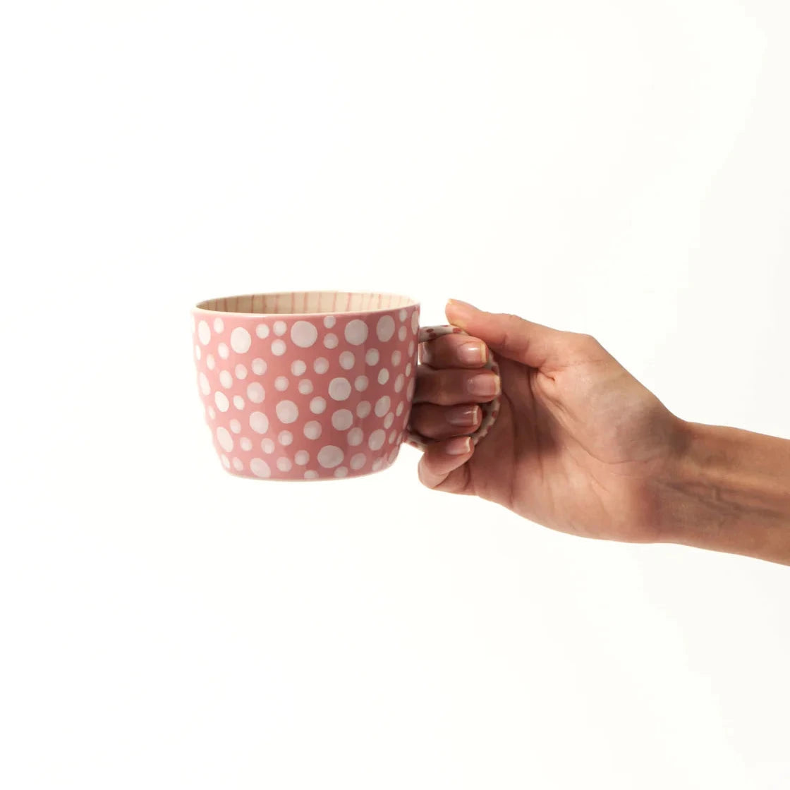 Hand holding a pink polka dot mug on a white background