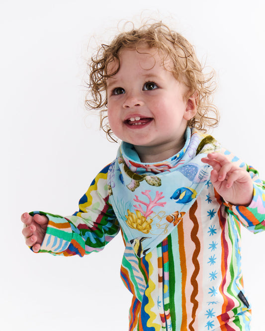 Child wearing a colorful outfit with the Reef Life design on a white background. The Reef Life pattern includes a sea turtle, angel fish, coral and many more marine life.