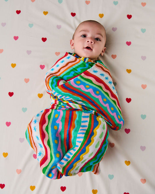 Baby wrapped in a colorful striped swaddle on a heart-patterned blanket