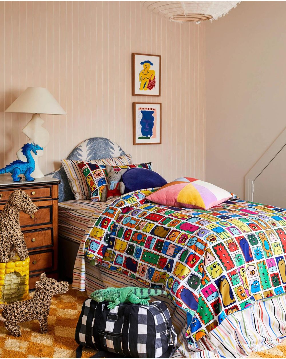 Kip & Co Black & White Gingham Duffle Bag on the floor of a bedroom next to a bed. There are various animal stuffies positioned near the bed, and a lizard shaped stuffy is on top of the bag.
