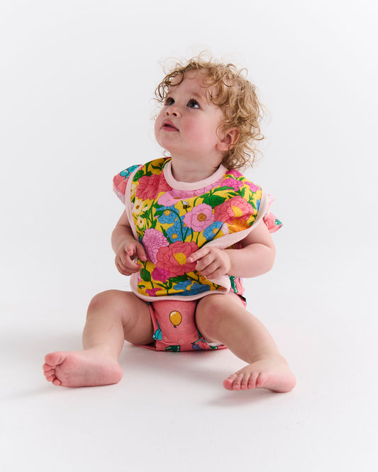 Child wearing a Follow The Sun Yellow Bib - a colorful floral bib, and diaper on a white background