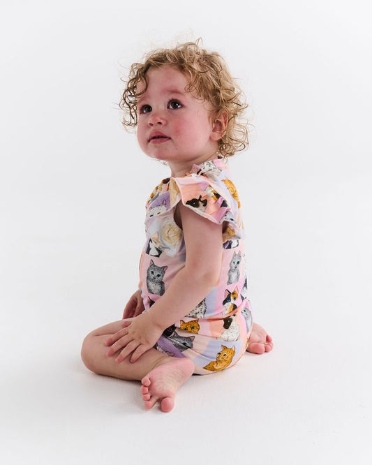 Child wearing a colorful romper with cat prints on a white background