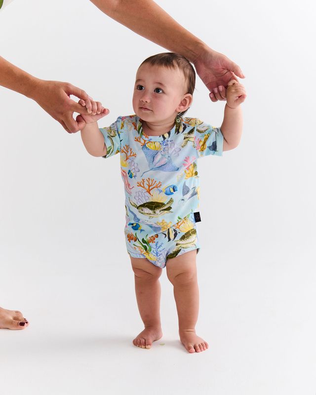 Baby in a colorful onesie with sea-themed design, standing on a white background