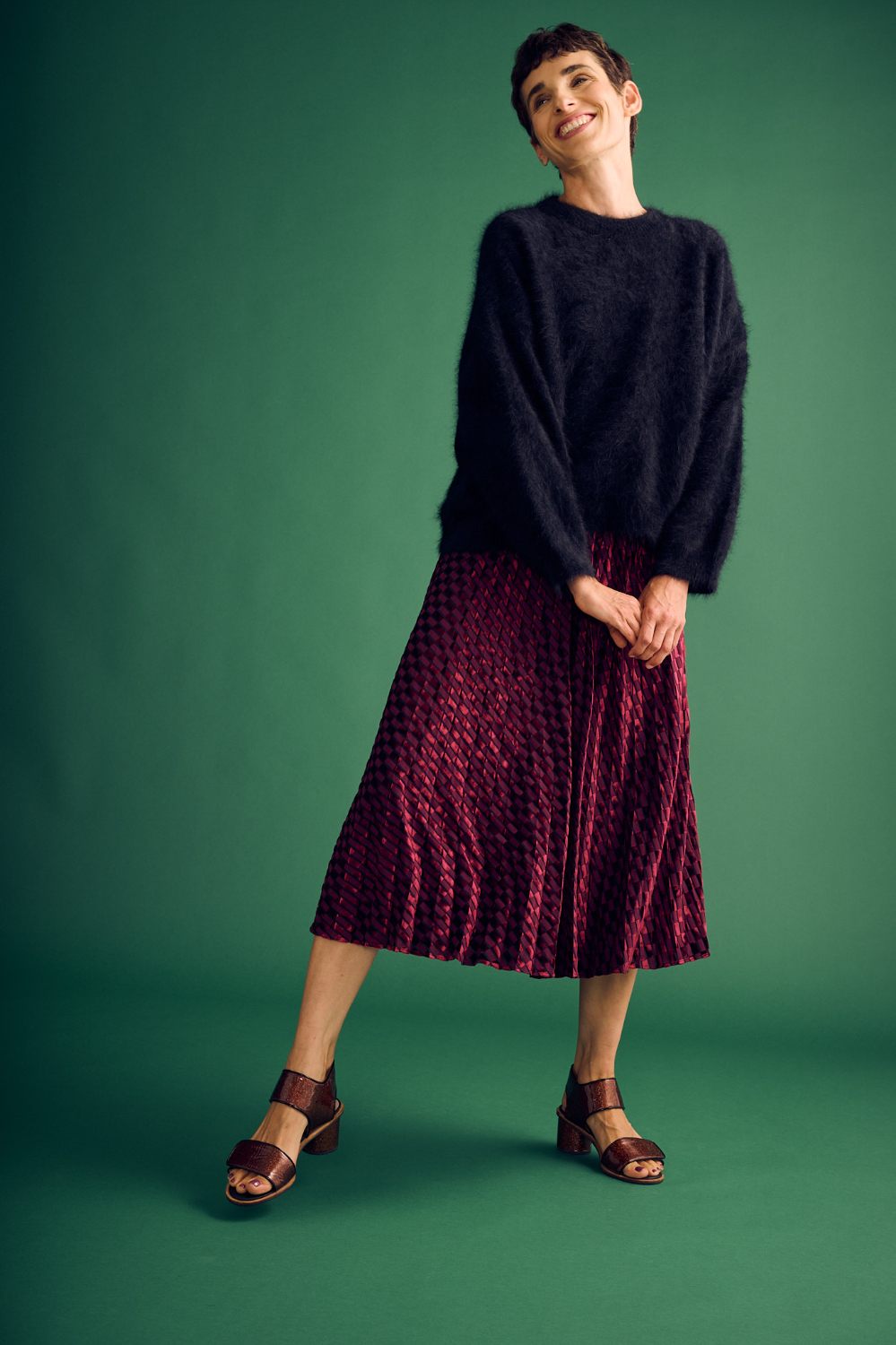 Woman wearing a black sweater and red patterned skirt on a green background