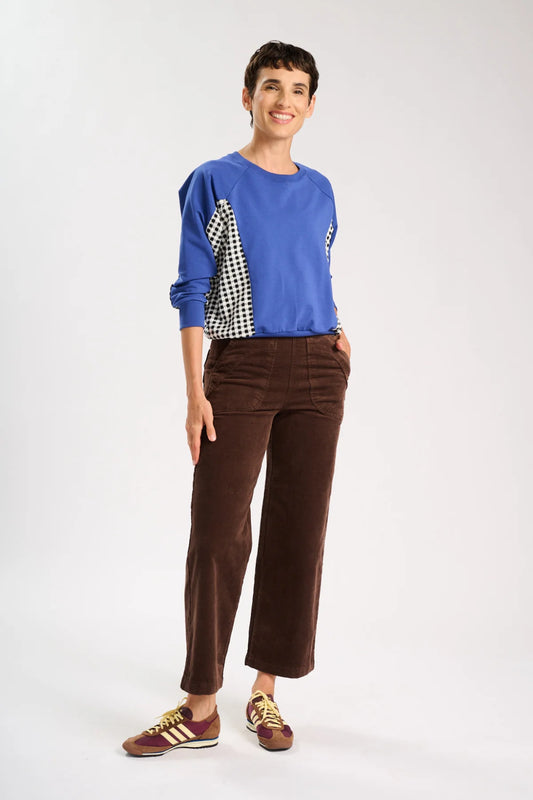 Model is standing and wearing a blue jumper and a pair of brown corduroy pants