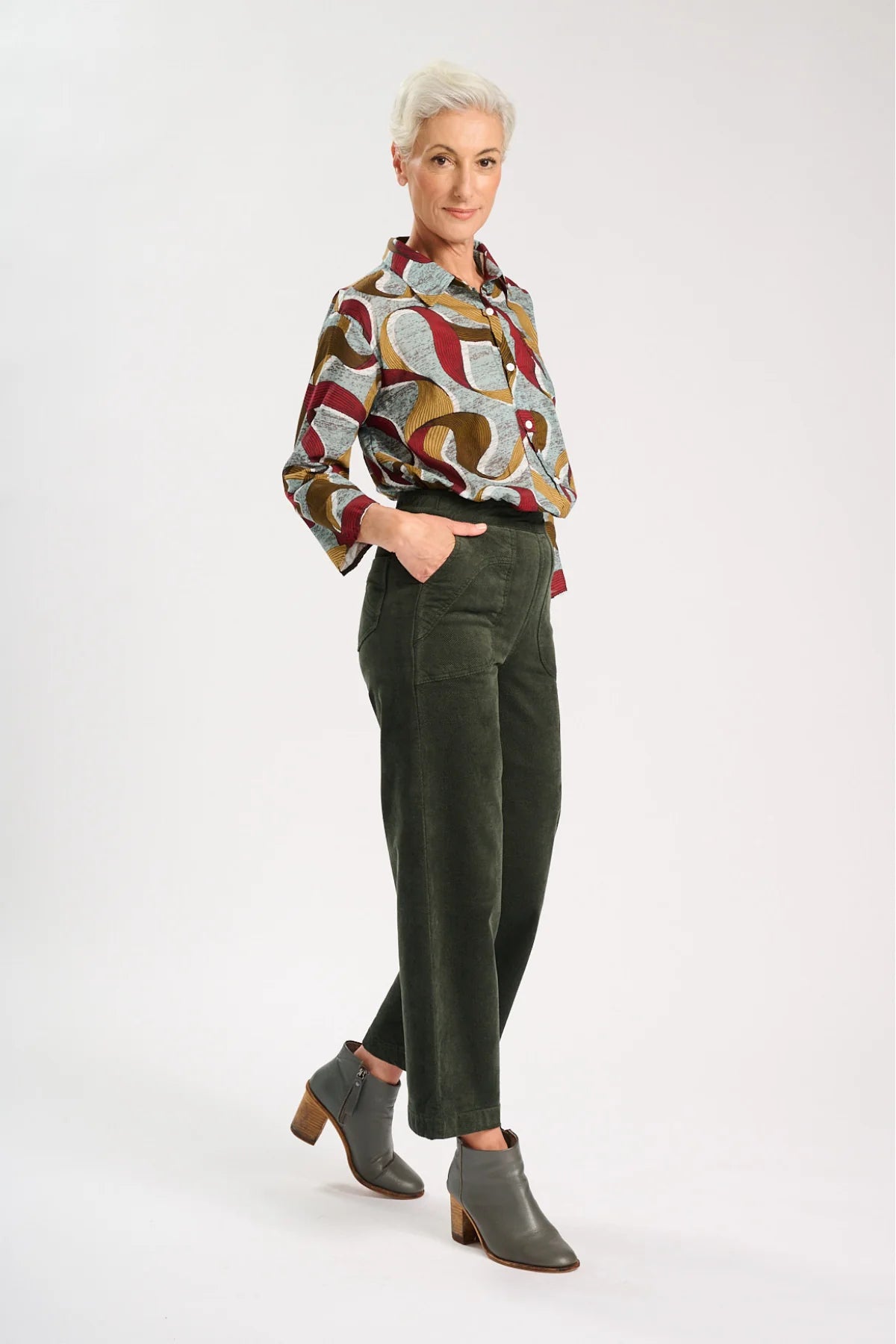 Side view of Model wearing Dark khaki green velvet pants with a colourful pattern shirt