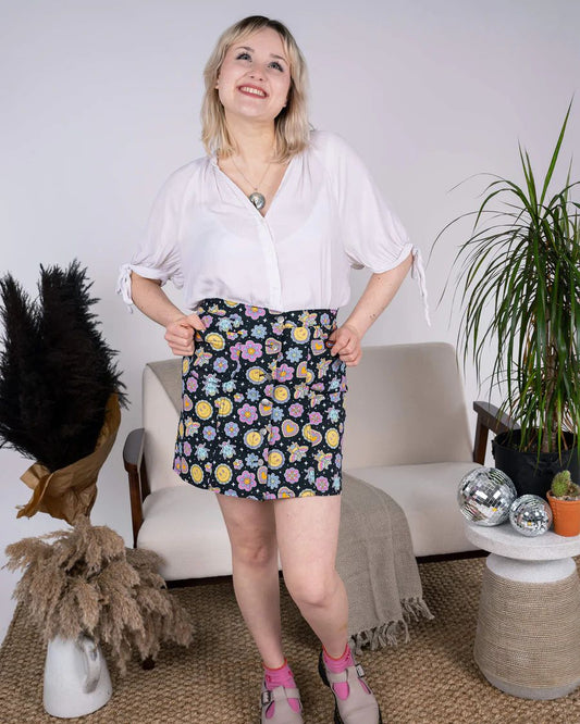 Model is wearing Run and Fly Bee Happy Mini Skirt. She is looking above the camera and smiling.