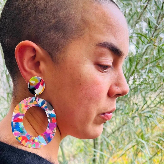 Person wearing colorful earrings with a blurred natural background