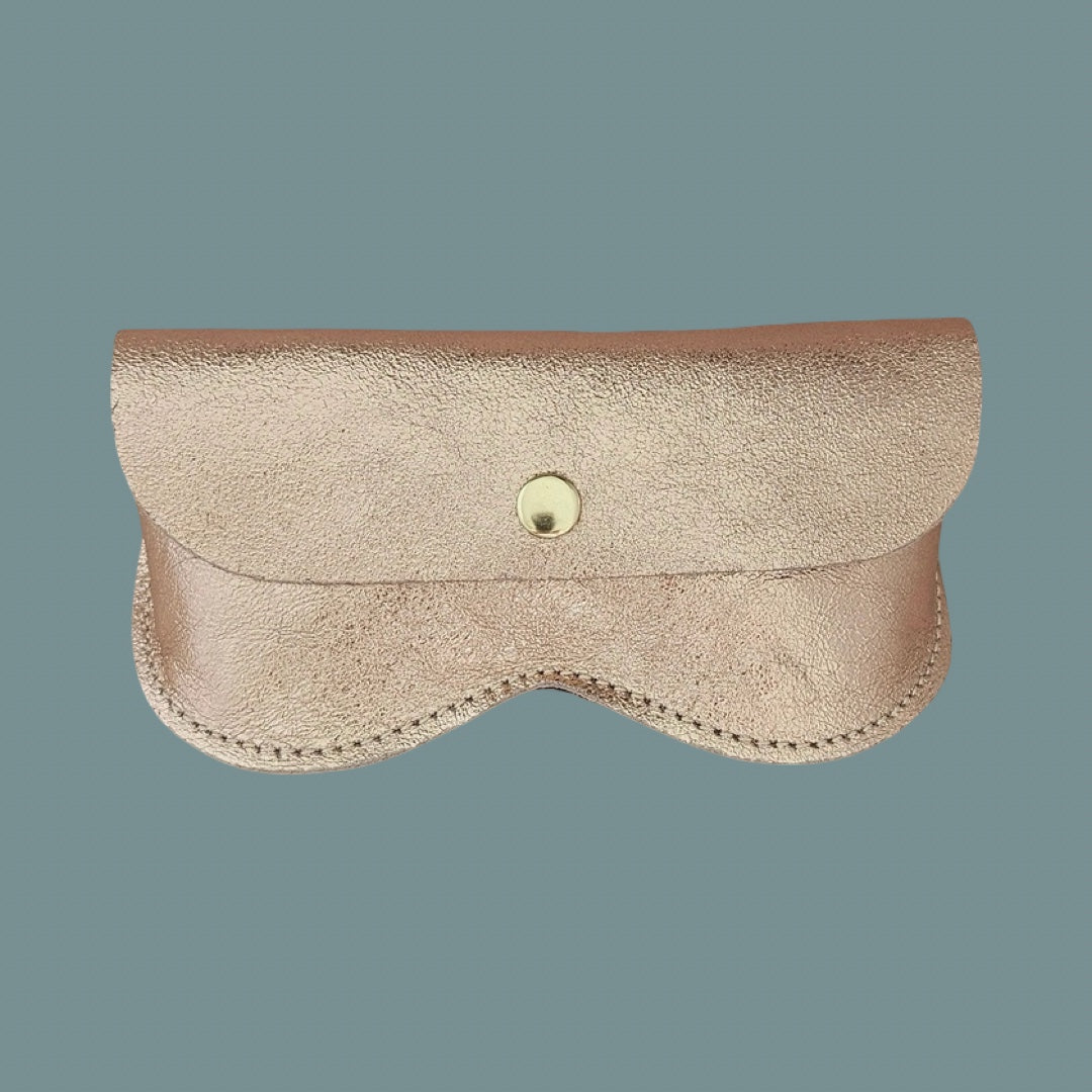 A light rose pink textured leather glasses case with a gold snap button closure, shown against a solid slate blue background.