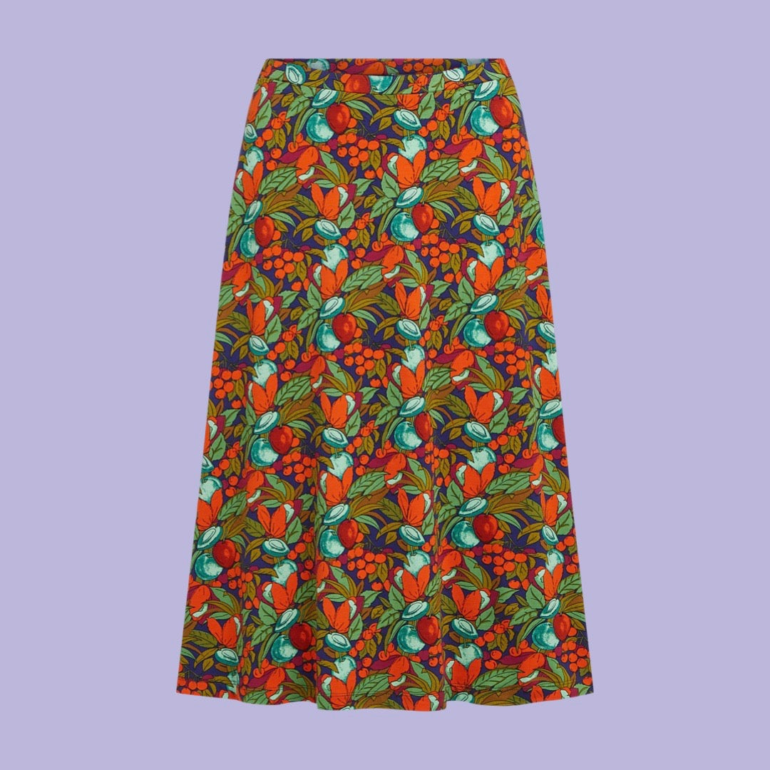 A knee-length A-line skirt with a dense, colorful botanical pattern featuring orange flowers, green leaves, and red berries on a dark background, shown flat against a solid lavender background.