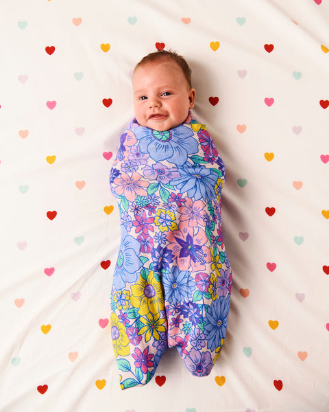 Styled image of Kip & Co Bunch of Fun Bamboo Baby Swaddle wrapped around a baby on a bed with hearts on the bedsheet.