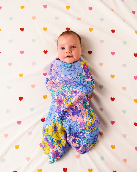 Styled image of Kip & Co Bunch of Fun Bamboo Baby Swaddle wrapped around a baby on a bed with hearts on the bedsheet.