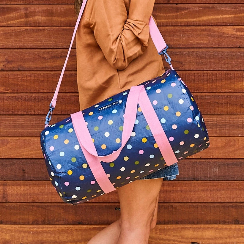 Person holding a blue duffel bag with colorful polka dots against a wooden background