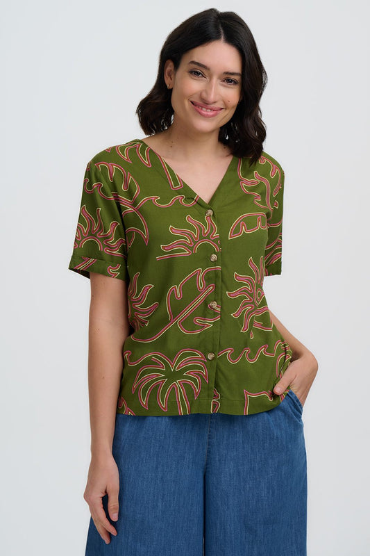 Woman wearing a green patterned blouse with blue pants on a white background