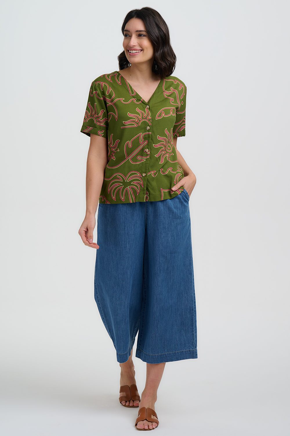 Woman wearing a green patterned top and blue pants on a white background