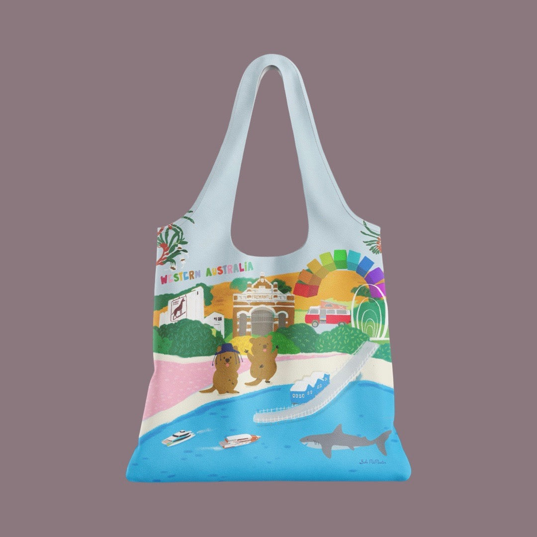A reusable tote bag with a light blue base and a colorful illustrated print of Western Australia, including a beach, buildings, a rainbow, and marine life, shown against a solid mauve background.