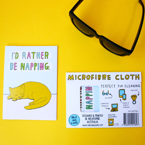 Flat lay of Able & Game I'd Rather Be Napping Microfibre Cloth with packaging sleeve and a pair of sunnies