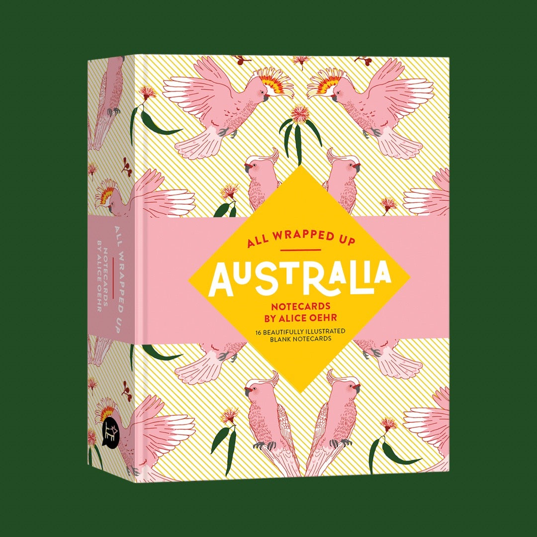 All Wrapped Up: Australia notecards box by Alice Oehr, featuring a pink and yellow cockatoo pattern with a central yellow diamond label, shown on a dark green background.