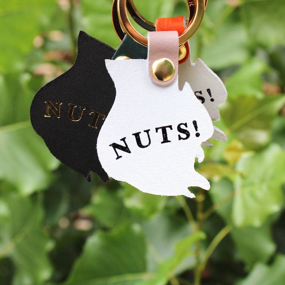 Keychain with black and white squirrel-shaped tags reading 'NUTS!' against a green leafy background