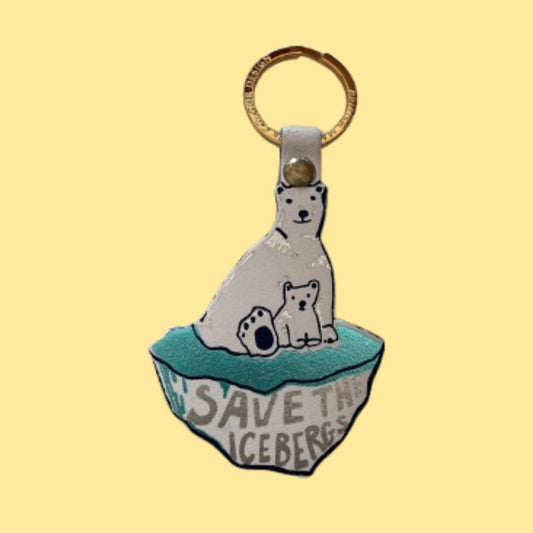 A handmade key chain shaped like an iceberg with a polar bear and polar bear cub on top. The pin features a white bear, a metallic teal iceberg base with the text 'SAVE THE ICEBERGS' in silver foil, and a gold-tone split ring at the top.
