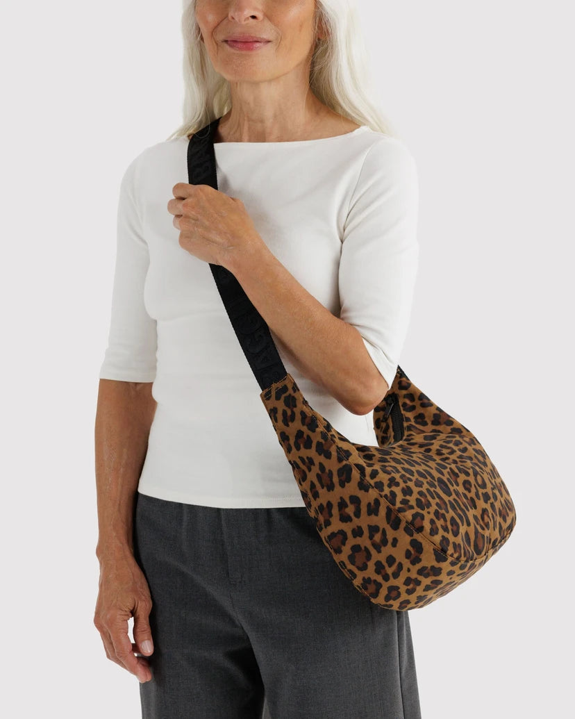 A woman wearing a white top and dark grey pants carries a leopard-print shoulder bag with a black strap against a white background.
