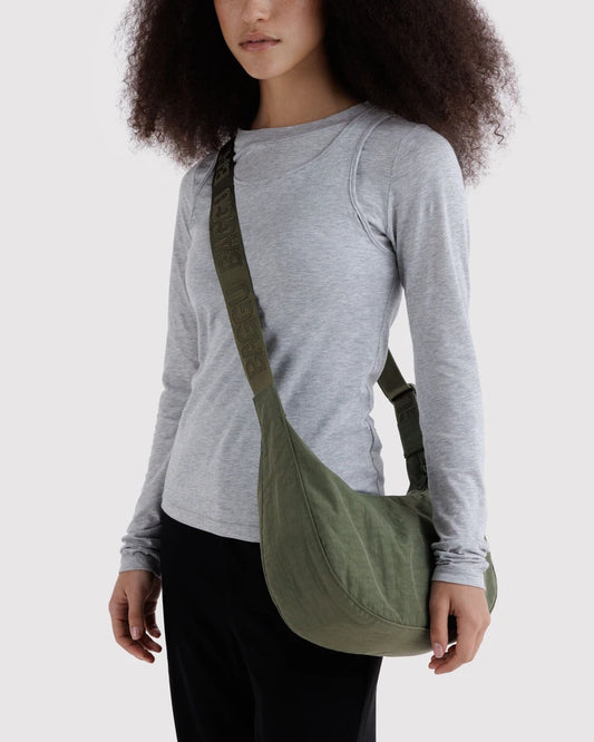 Person wearing a gray long-sleeve shirt with a green crossbody bag on a white background