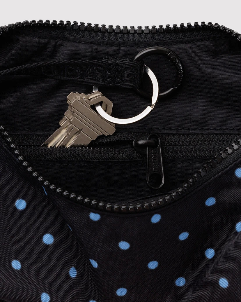 Close-up of a black nylon bag with light blue polka dots, showing a zipper opening with a metal keyring and keys inside.