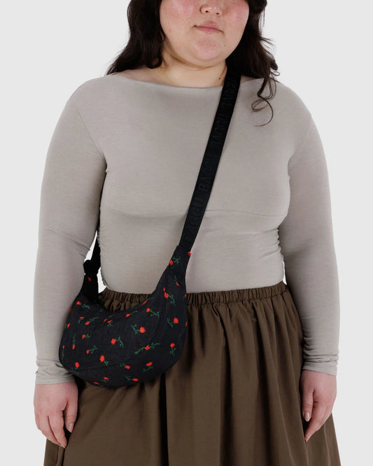 Person wearing a black crossbody bag with red flowers and green stems on a plain background