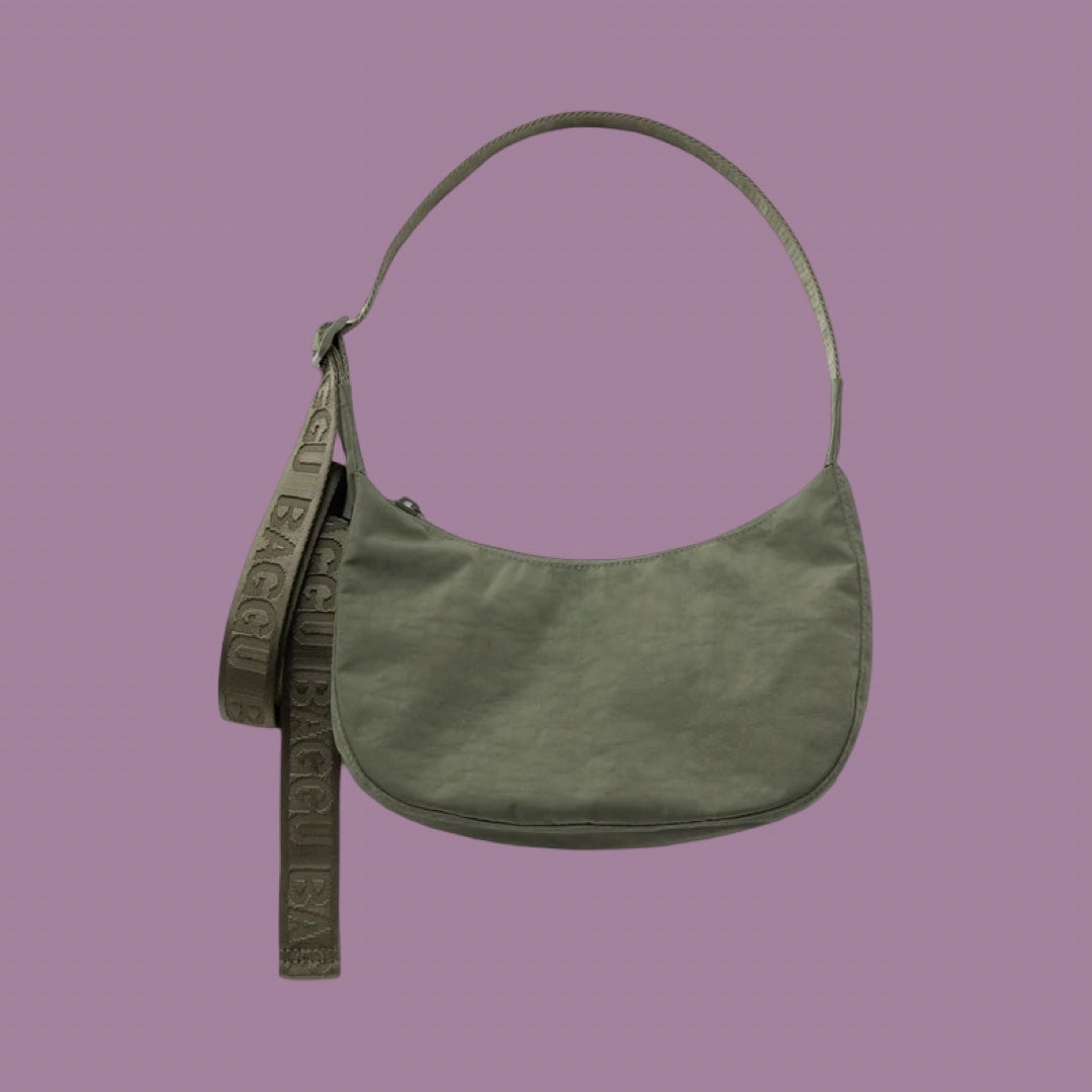 Baggu Small Crescent Bag in Caper. An olive green shoulder bag with a matching fabric strap featuring embossed text, displayed against a solid mauve background.