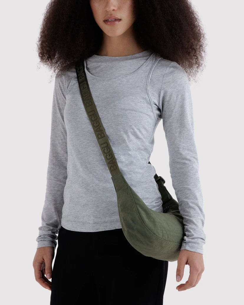 Person wearing a gray long-sleeve shirt and carrying a green crossbody bag on a white background
