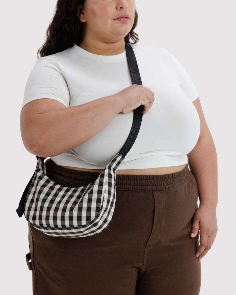 Person wearing a white top and brown pants with a black and white checkered bag over their shoulder on a white background