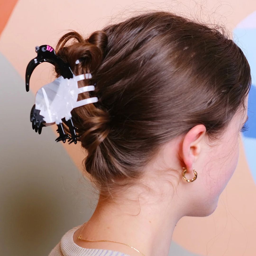 A woman shown from the back wearing an Ibis Bin Chicken claw-style hair clip with black accents and small pink details, holding her brown hair in a low bun.