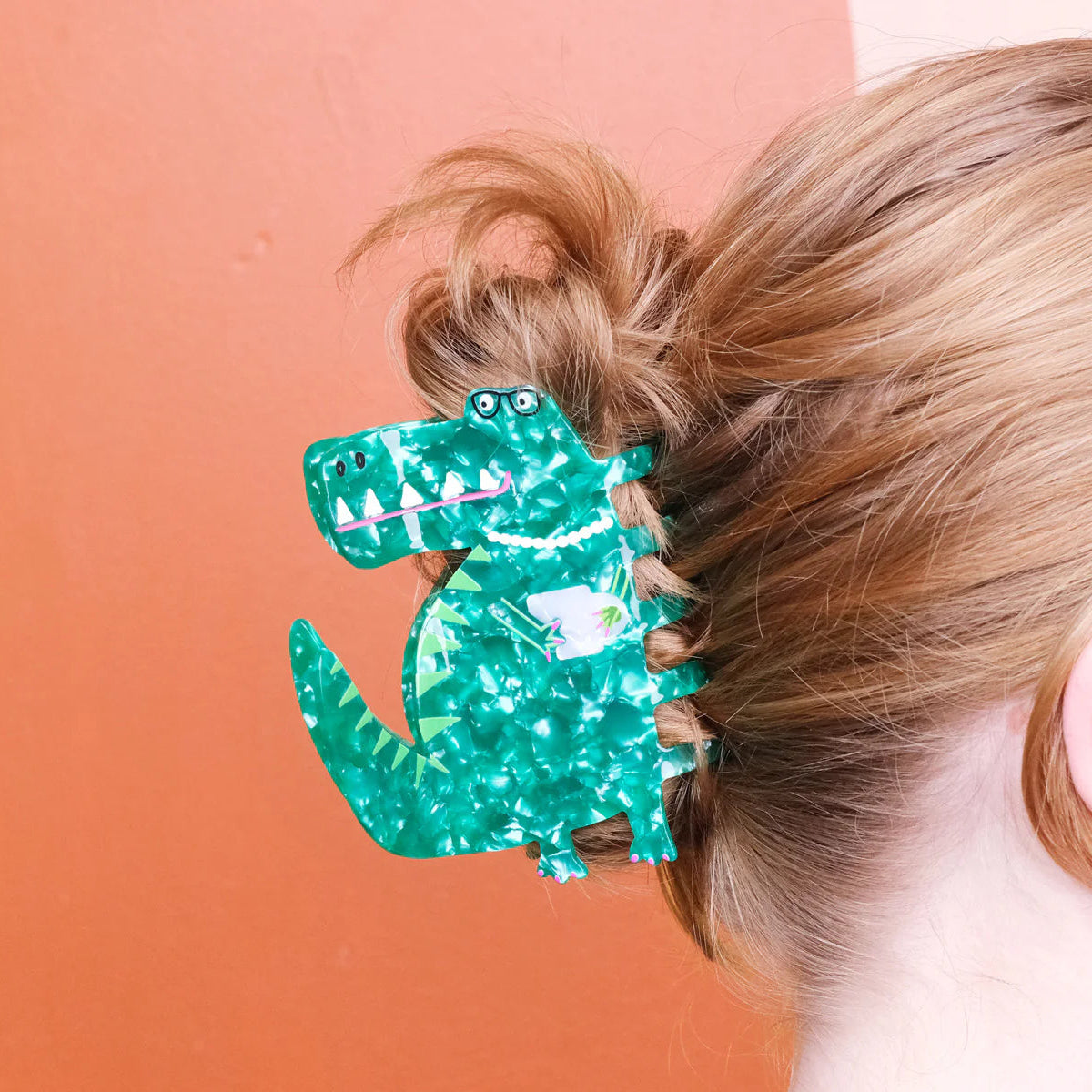 Person with a green dinosaur-shaped hair clip in their hair against an orange background