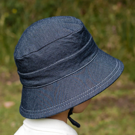Side view of Blue-black denim bucket hat worn by a child against a blurred natural background