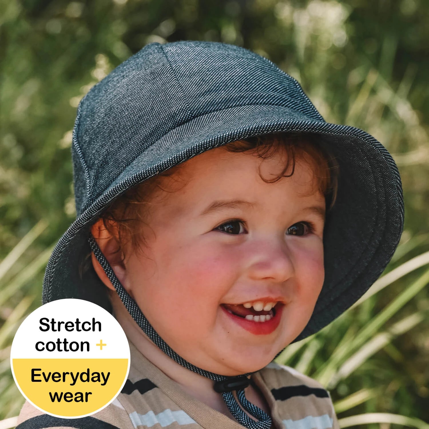 Toddler wearing a denim hat with a green blurred background
