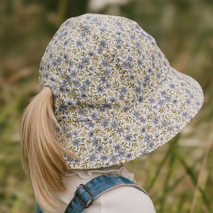 Back view of Child wearing a floral-patterned hat with a ponytail slit in the back in a natural setting