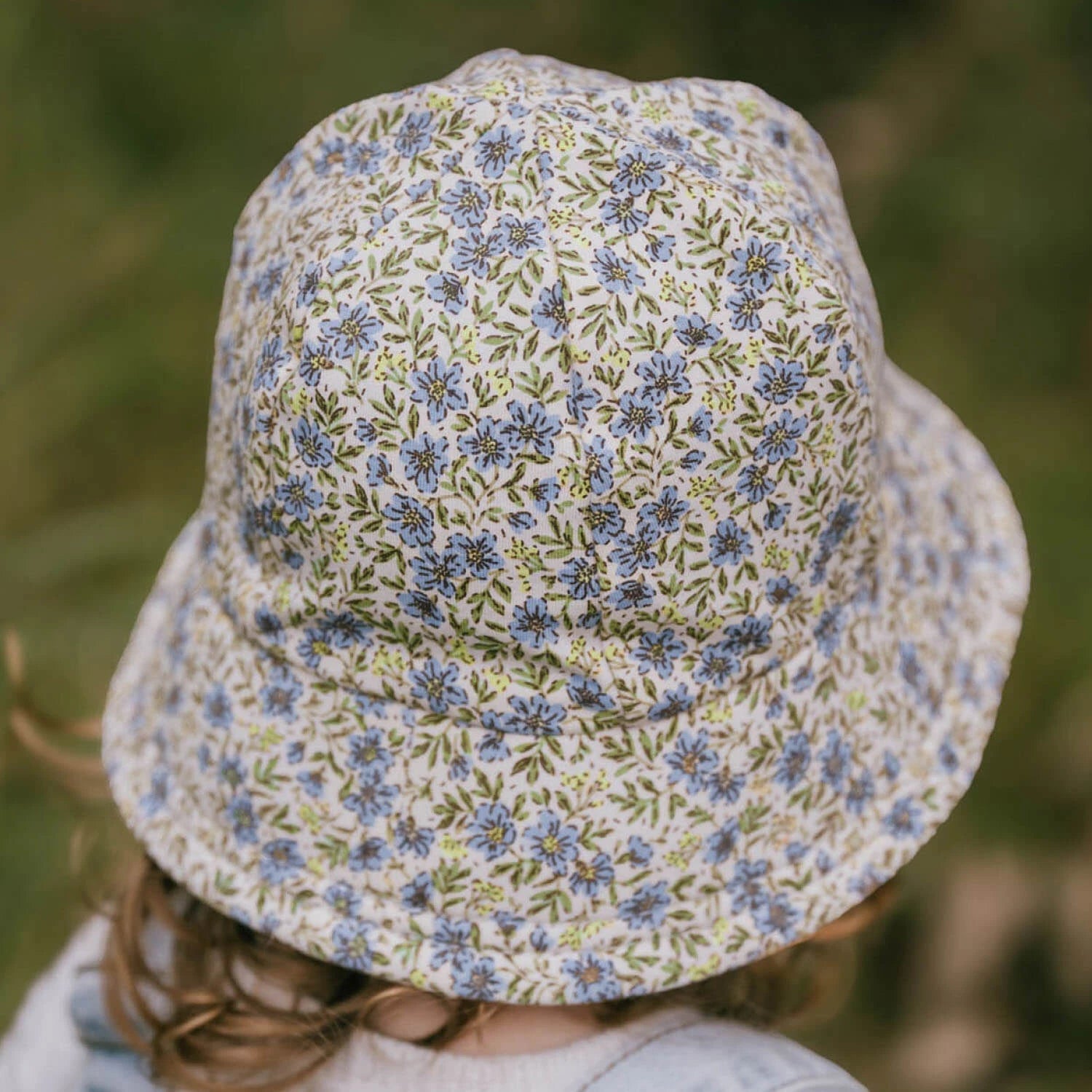 Back view of Floral-patterned bucket hat worn by a toddler with a blurred natural background
