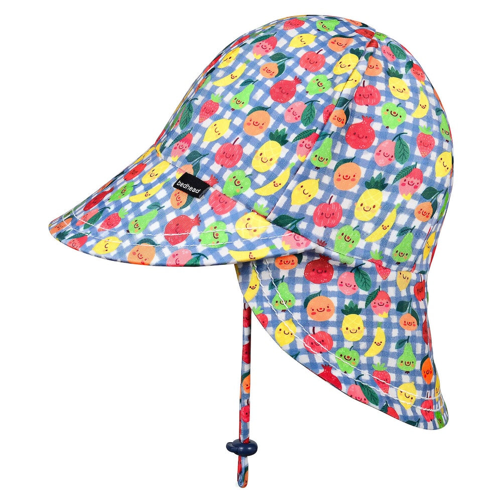 A children's swim hat with a blue and white gingham pattern and a colourful print of smiling cartoon fruits, including pineapples, strawberries and oranges. It features an adjustable chin strap with a dark blue toggle.