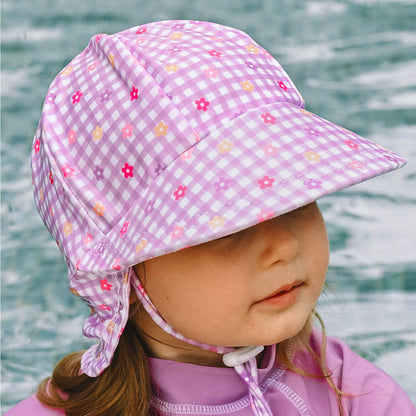 A child wearing a pink and white gingham swim hat with small floral prints, photographed outdoors with a pool in the background.